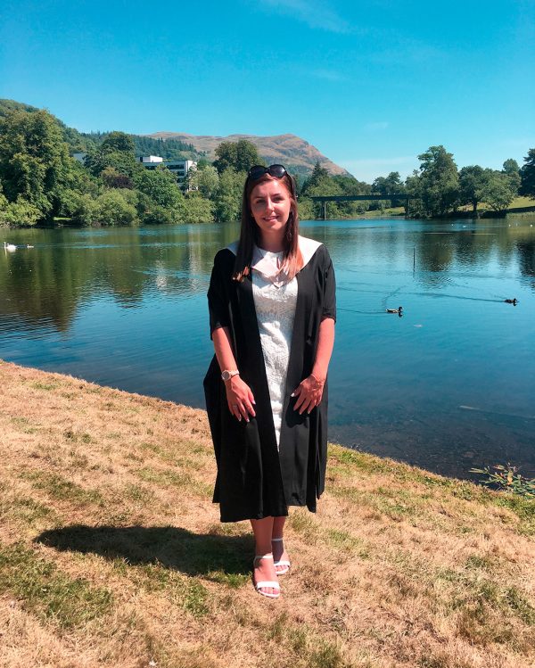 Lucy Walkup in graduation gown infront of a loch