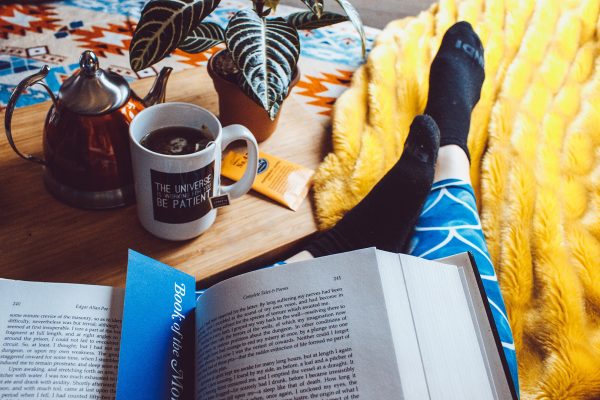 Person relaxing at home, drinking tea and reading a book looking after their mental health