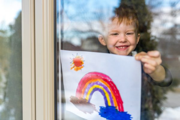 Young Boy sticking his drawing on home window during the Coronavirus Covid-19 crisis, Many people are putting a rainbow to tell neighbors that people inside this house are ok. #Stay at home.